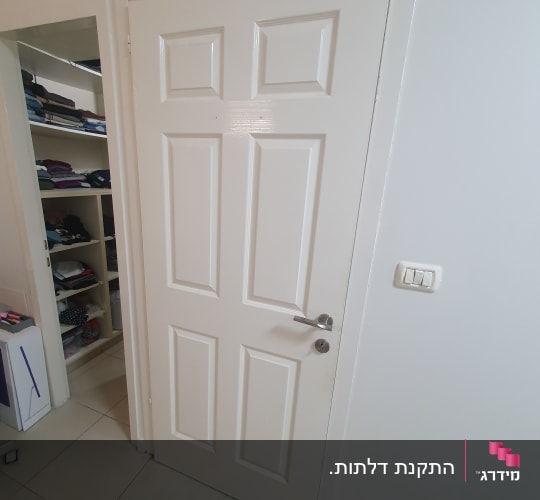 דלת לבנה עם ידית מתכת ומתג חשמל